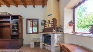 A living room with a fireplace, wooden furniture, a window with a view, and a tiled floor. - Holiday Home "Villa Gabri" with Pool, Garden & Terrace (Carlentini)