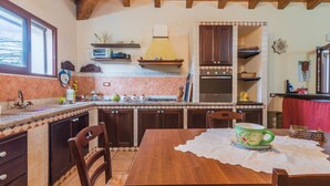 A kitchen with wooden cabinets, a stove, and a dining table with chairs. - Holiday Home "Villa Gabri" with Pool, Garden & Terrace (Carlentini)