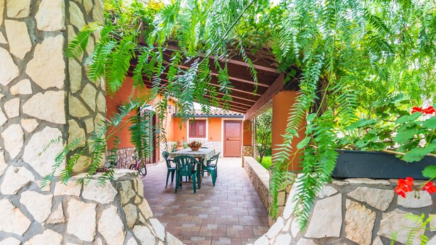 A stone-walled patio with a table and chairs, surrounded by greenery and a pergola. - Holiday Home "Villa Gabri" with Pool, Garden & Terrace (Carlentini)