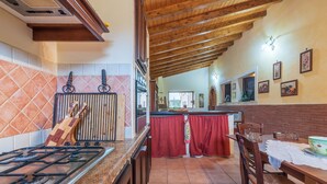 A kitchen with a gas stove, wooden cabinets, a tiled backsplash, and a dining area with a table and chairs. - Holiday Home "Villa Gabri" with Pool, Garden & Terrace (Carlentini)