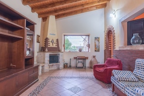 A living room with a fireplace, wooden furniture, a red chair, and a patterned sofa. - Holiday Home "Villa Gabri" with Pool, Garden & Terrace (Carlentini)