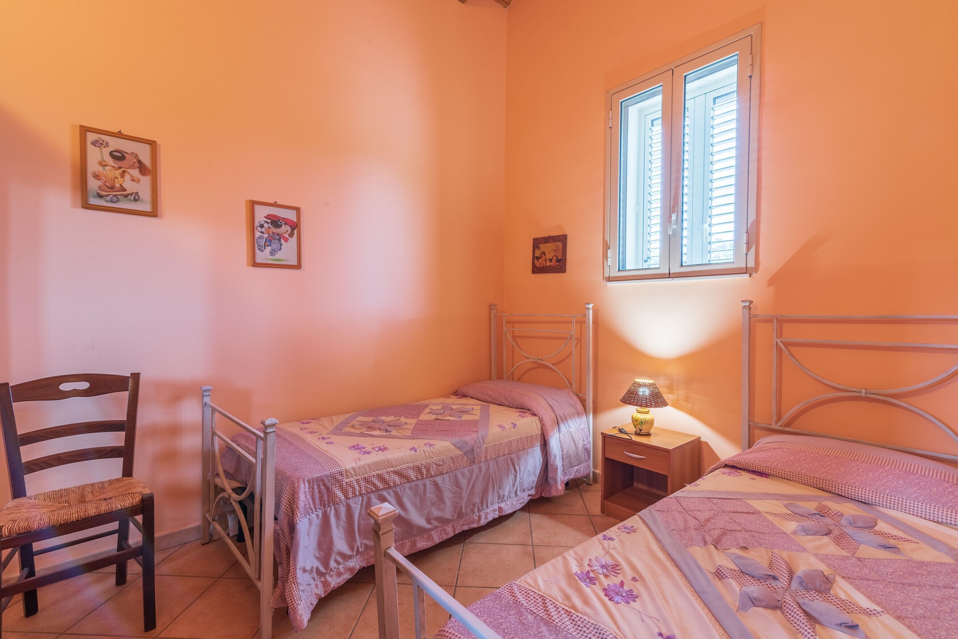Ein Schlafzimmer mit zwei Einzelbetten, einem Sessel, einem Nachttisch mit Lampe und gerahmten Bildern an der Wand.