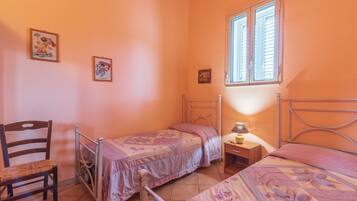 Ein Schlafzimmer mit zwei Einzelbetten, einem Sessel, einem Nachttisch mit Lampe und gerahmten Bildern an der Wand.