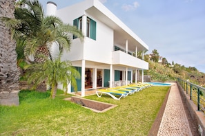 Una casa moderna de dos pisos con piscina, mobiliario exterior y un camino de piedra.