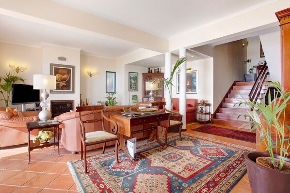 A spacious living room with a fireplace, a large rug, and a staircase leading to an upper floor.
