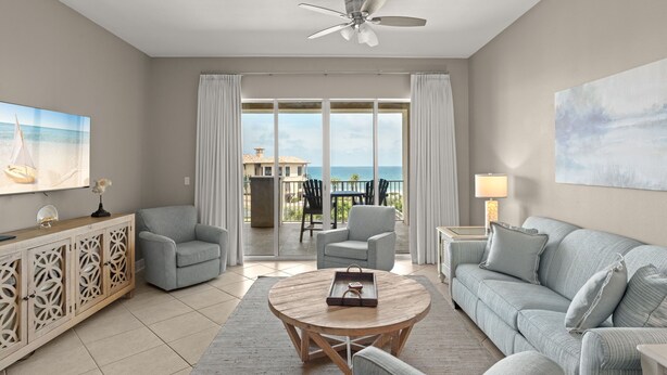 A living room with a round coffee table, two armchairs, a sofa, a ceiling fan, a large window with curtains, and a painting on the wall. - Gulf and Pool Views, Free Seasonal Beach Service, Designated Beach Area on 30A!! (Santa Rosa Beach)