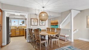 A dining area with a round table, wooden chairs, and a hanging light fixture. - Gulf Front Townhome, Downtown Destin! (Destin)