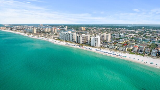 An aerial view of a coastal city with a beach, high-rise buildings, and a clear sky. - Gulf Front Townhome, Downtown Destin! (Destin)