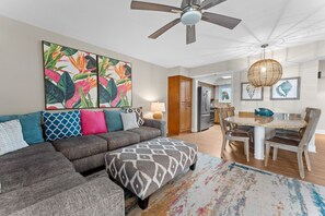 Un salon moderne avec un canapé d’angle, une table à manger avec des chaises et un ventilateur de plafond.