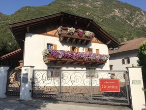 A two-story building with balconies adorned with flowers, a gated entrance, and a sign indicating 'Apartments Giustina'.