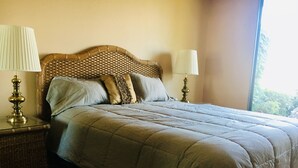 Una cama bien tendida con cabecera, dos lámparas de noche y vistas al exterior con vegetación.