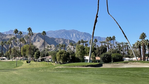Un campo de golf con palmeras y montañas al fondo.