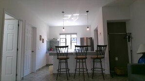 Una cocina moderna con una isla central, taburetes de bar, iluminación colgante y vistas a través de un ventanal.