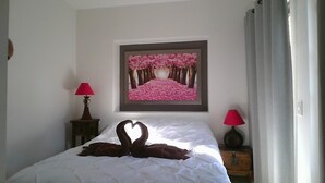 Un dormitorio con cama, dos lámparas de noche, un cuadro enmarcado de un sendero rosado y una ventana con cortinas.