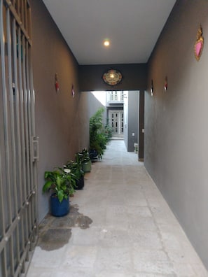 A corridor with potted plants, a metal gate, and a ceiling light fixture.