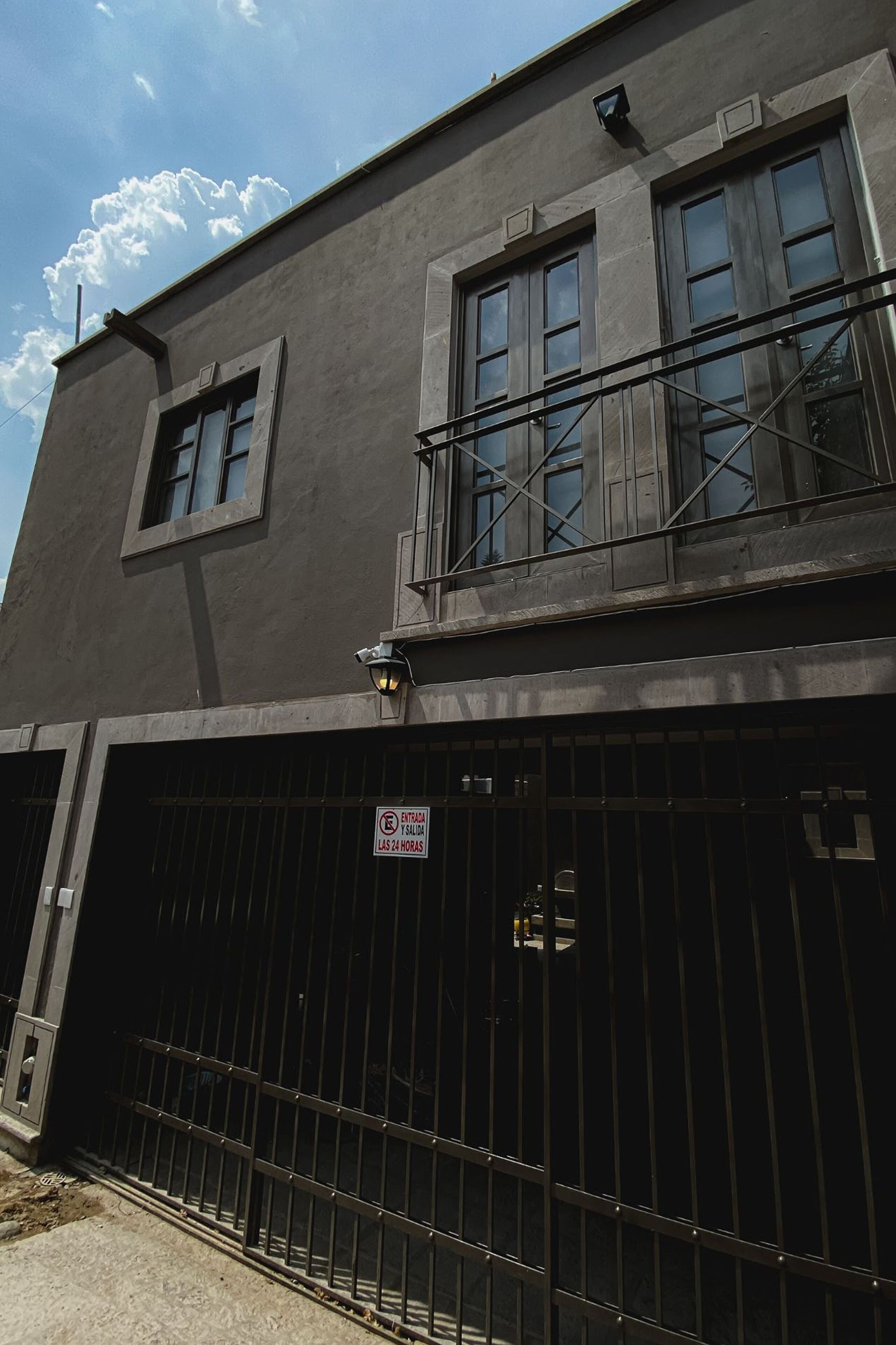 Un edificio con entrada protegida por una reja, un balcón y un letrero que indica horarios de acceso restringido.