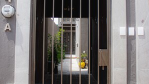 Una entrada de edificio con una puerta metálica, una placa con número y un cuadro eléctrico.