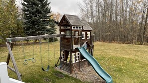 Een houten speeltuintje met een glijbaan en schommels in een achtertuin.
