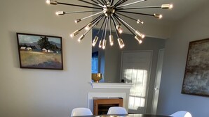 A dining area with a round table, white chairs, a modern chandelier, and artwork on the walls. - Coastal Condo w/Great Amenities, Walkable to Beach (Dana Point)