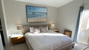 A bedroom with a bed, bedside tables, a ceiling fan, a large window with curtains, and a beach-themed wall art. - Coastal Condo w/Great Amenities, Walkable to Beach (Dana Point)