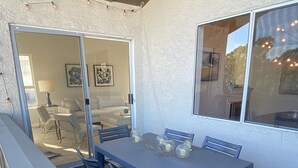 An outdoor patio with a table and chairs, a sliding glass door leading to an interior space, and string lights. - Coastal Condo w/Great Amenities, Walkable to Beach (Dana Point)