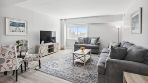 Ett modernt vardagsrum med en grå soffa, en mönstrad fåtölj, ett soffbord och en tv som står på ett träskåp.