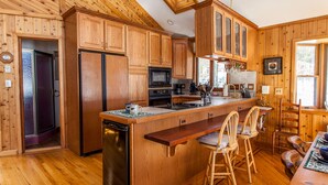 Una cocina tipo cabaña de madera con una isla central, armarios de madera, un refrigerador, un microondas y un fregadero.