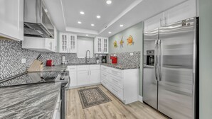 A modern kitchen with white cabinets, a stainless steel refrigerator, and a backsplash with a mosaic tile pattern.