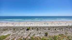 A beach with a fence in the foreground, a clear sky, and the ocean in the background.