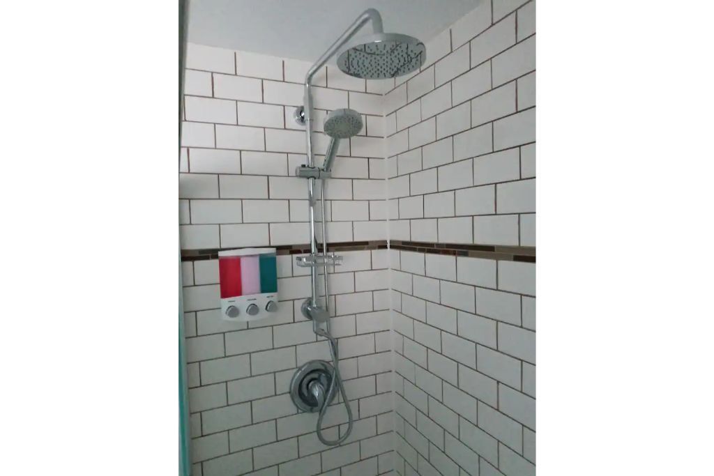 A shower with a handheld showerhead and a fixed showerhead, a control panel with multiple buttons, and a tiled wall.