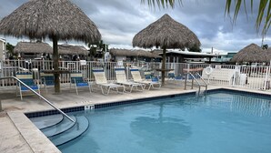 Une piscine dotée de chaises longues et de parasols en chaume.