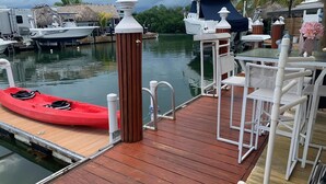 Une jetée en bois avec un kayak rouge, des chaises blanches et une petite table.