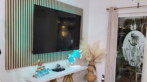 Un salon moderne doté d’un grand téléviseur à écran plat fixé au mur, lequel est recouvert de lambris en bois verticaux.