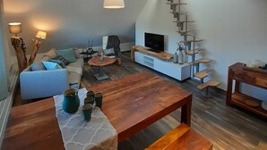 Ein modernes Wohnzimmer mit einer Holztreppe, einem Sofa, einem Couchtisch und einem Fernseher.