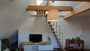 Ein Loft-Wohnzimmer mit einer Holztreppe, einem Fernseher und einem Essbereich.