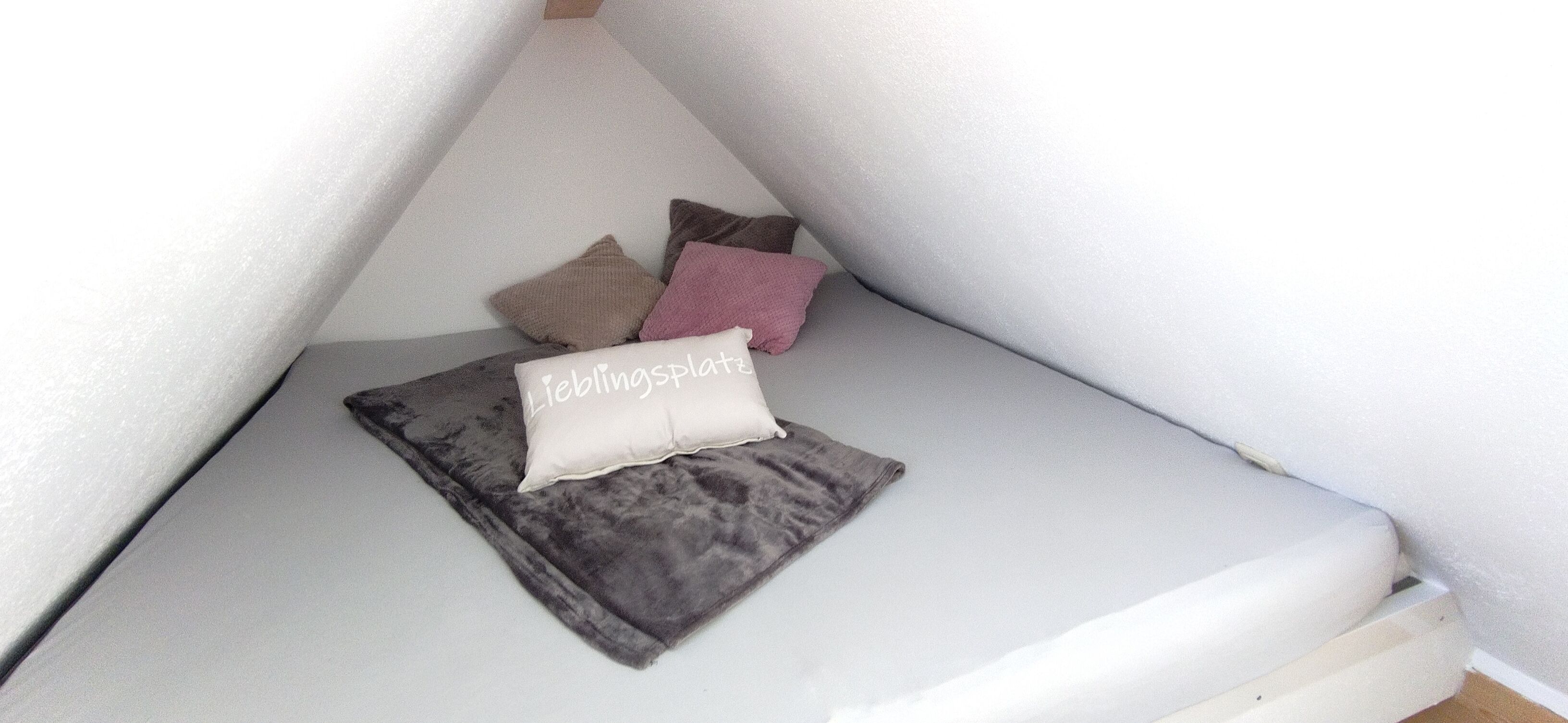 A corner of a room with a grey cushioned bench and several pillows in various colors.
