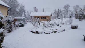 Ein mit Schnee bedeckter Garten mit einem Holthaus, einer Metalllaube und einer Steinmauer.