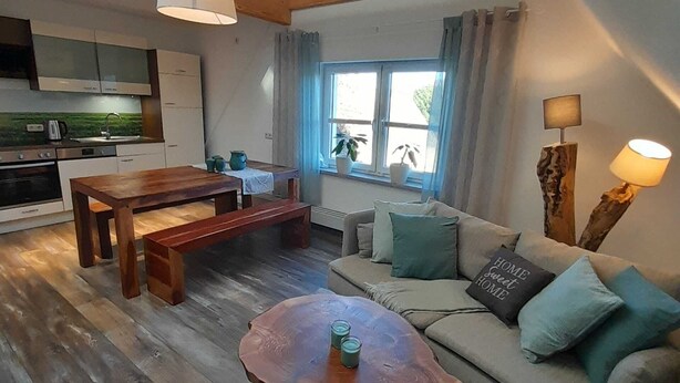 Ein modernes Wohnzimmer mit einem Holzesstisch, einer Couch mit Kissen, einem Couchtisch und einer Küche im Hintergrund.