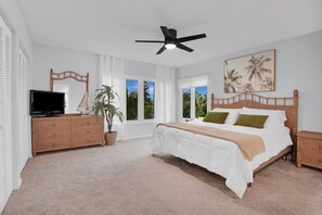 A bedroom with a bed, a television on a stand, a ceiling fan, and a window with curtains.
