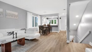 A modern living room with a white sofa, a glass coffee table, and a dining area with a wooden table and chairs.