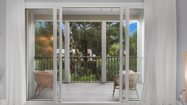 A room with a sliding glass door leading to an outdoor balcony with wicker chairs and a wooden deck.