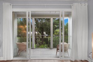 A room with a sliding glass door leading to an outdoor balcony with wicker chairs and a wooden deck.