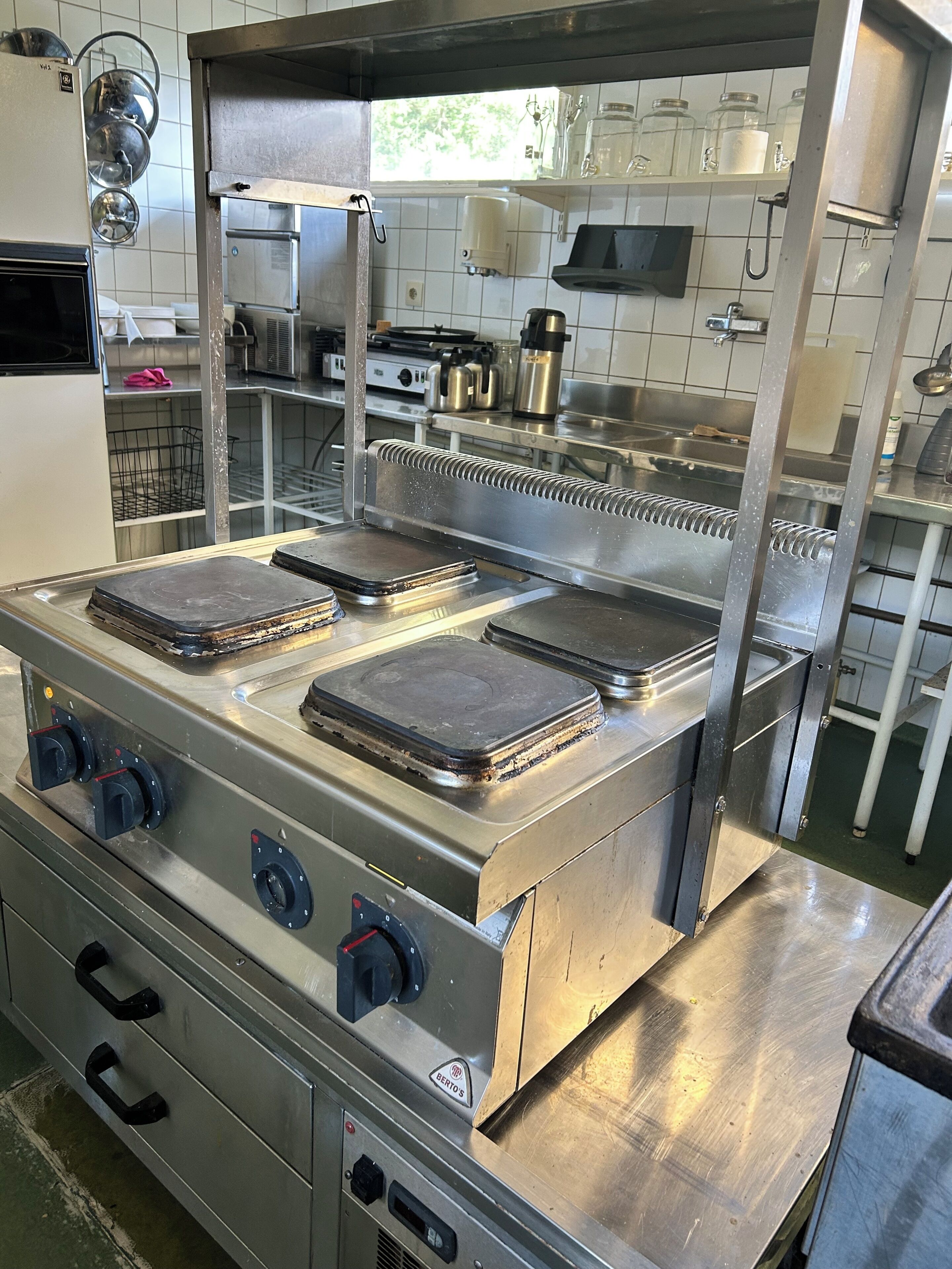Cocina comercial con electrodomésticos de acero inoxidable, incluyendo una estufa grande con múltiples hornillas y una campana extractora.