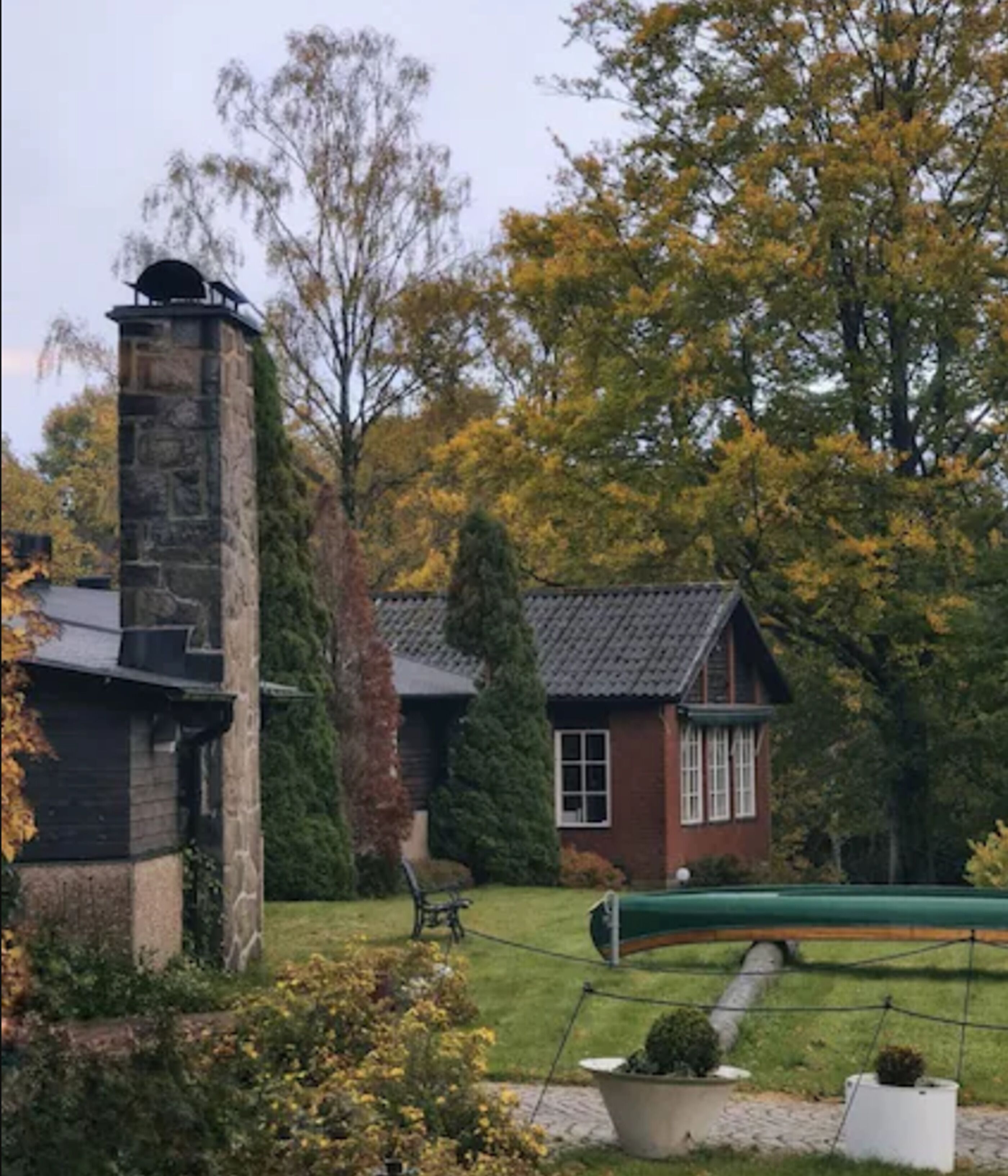 Een stenen schoorsteen, een klein huisje van baksteen met een raam, en een groene boot in een tuin.