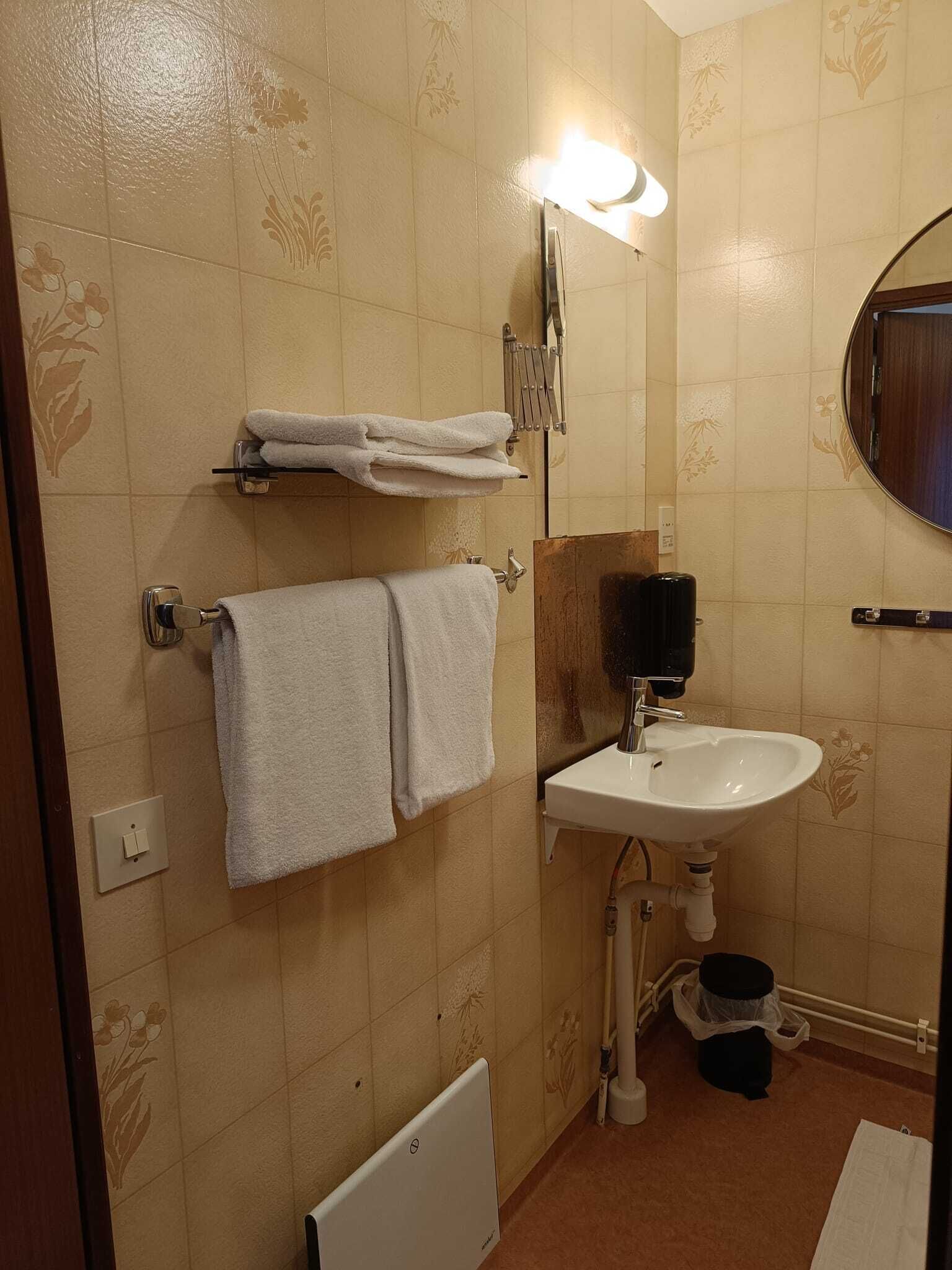 A bathroom with a white sink, a towel rack with folded towels, a mirror, and a light fixture.