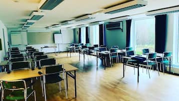 Ett rymligt konferensrum med flera rader av bord och stolar, stora fönster och en whiteboard.