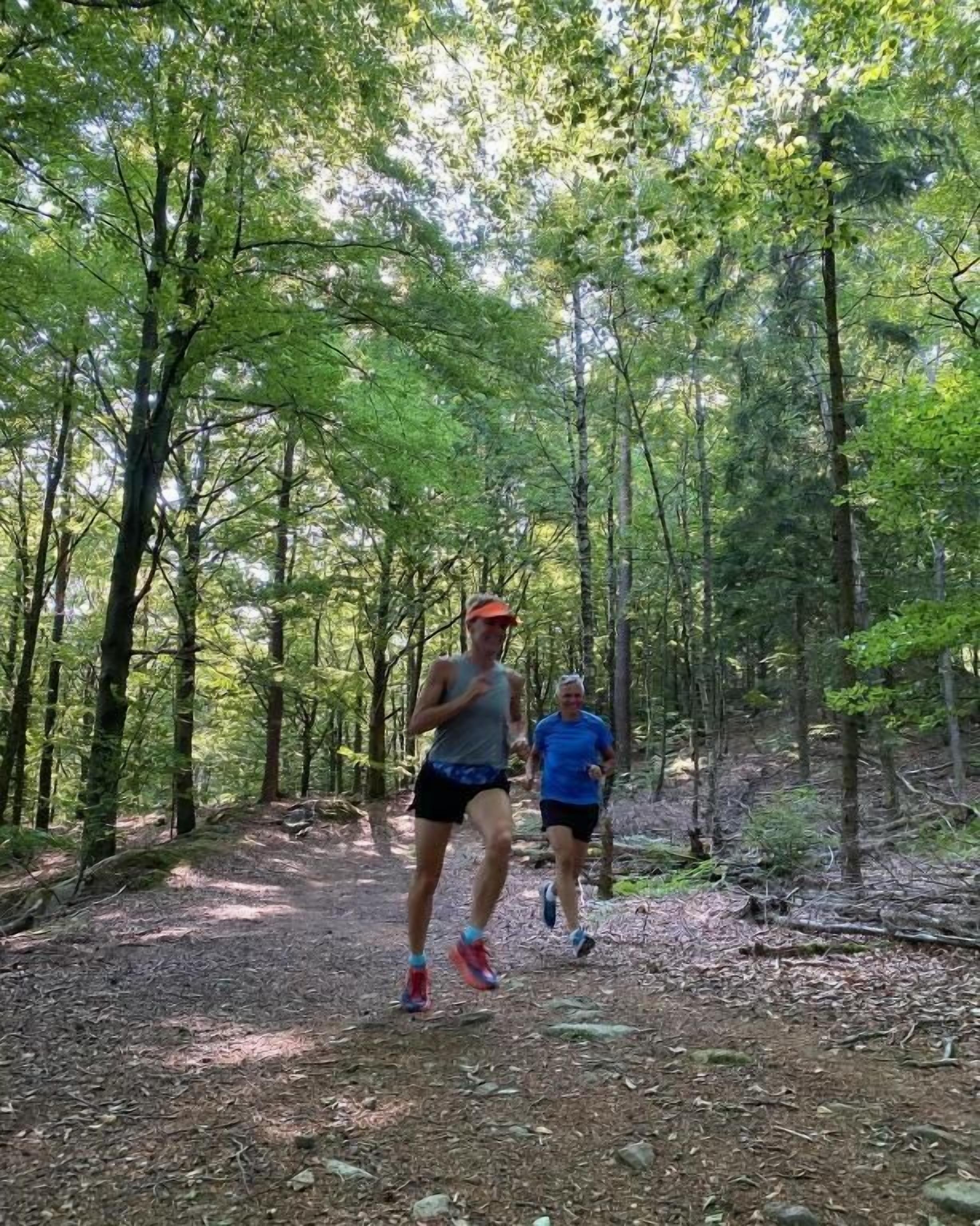 Duas pessoas correndo por uma trilha na floresta.