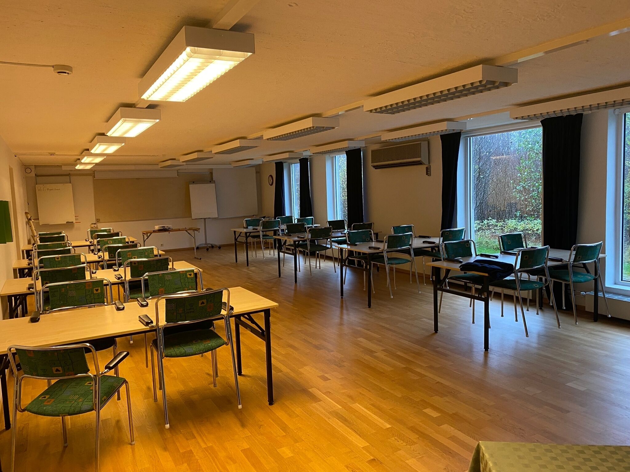 A classroom with rows of desks and chairs, large windows, and a whiteboard.