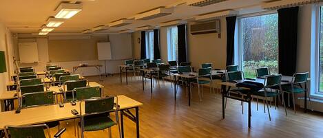 A classroom with rows of desks and chairs, large windows, and a whiteboard.