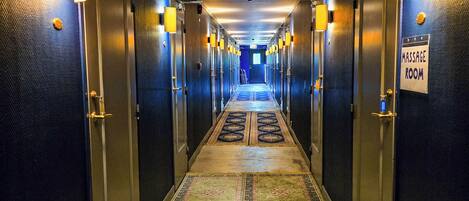 A hotel hallway with a carpeted floor, doors on both sides, and a sign indicating a massage room.